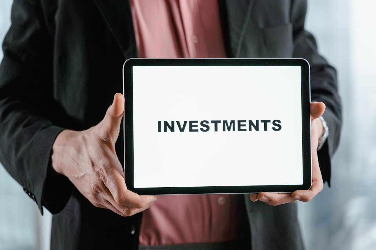 about-02 A businessman in a suit holds a tablet displaying the text 'INVESTMENTS'.